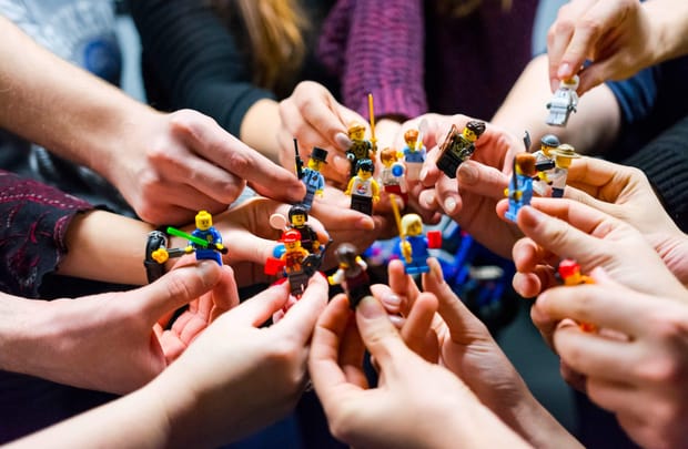 Many hands holding tiny Lego figures in a variety of outfits and holding different tools.
