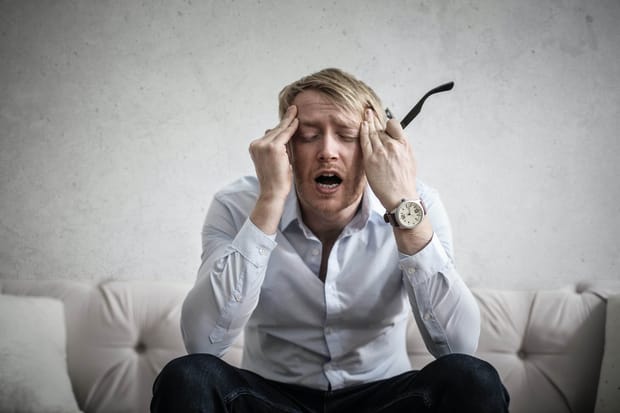 Man in business attire holding his classes and rubbing his temples.