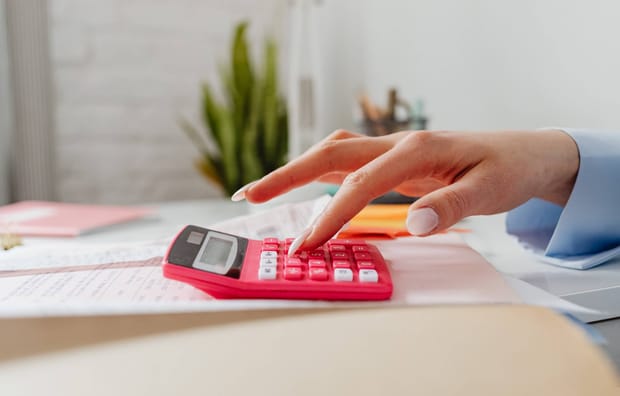 Photo of woman's hand using a light red calculator resting on a desk.