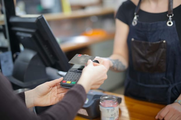 Close-up photo of a shop worker holding a debit card reader while a customer makes a payment