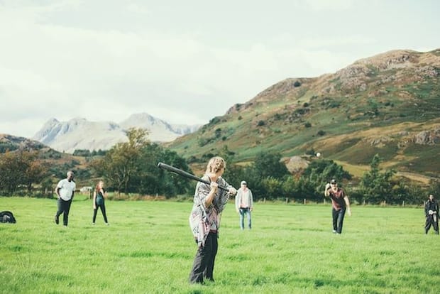 Group of people playing rounders outside on the grass with hills in the background