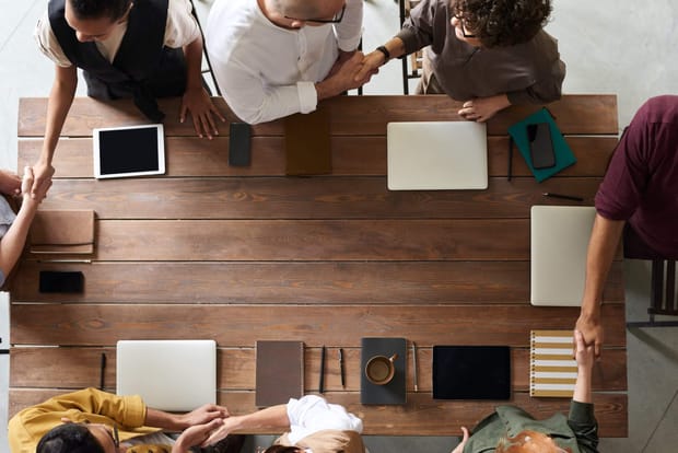 Top-down photo of coworkers around a rectangular wooden table shaking hands