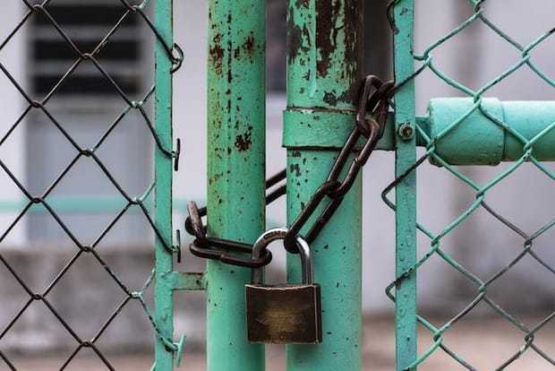 Rusted green metal gate locked shut with a chain and padlock