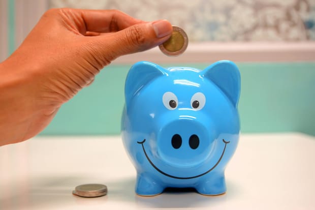 Photo of a hand placing a coin into a blue piggy bank with a smiling face