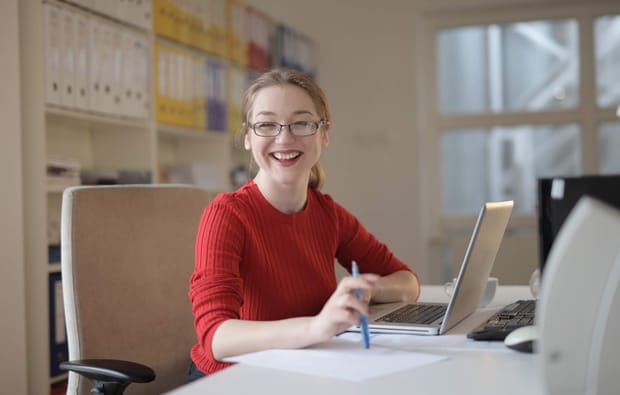 Woman wearing a red sweater smiling while working at a laptop