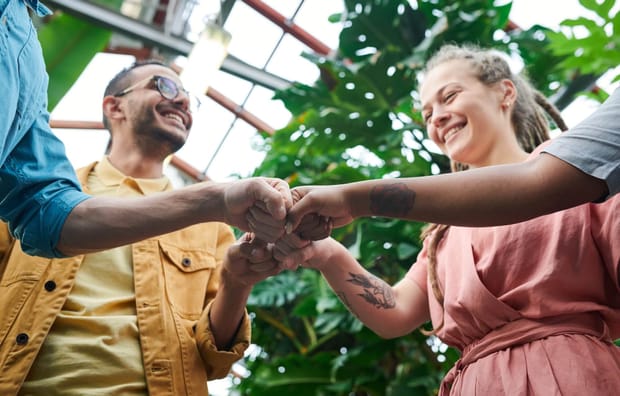 Close-up photo of four people, two in frame, fist-bumping while smiling