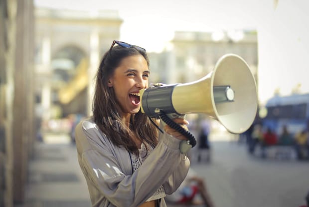 Photo of a young woman smiling while speaking into a large megaphone