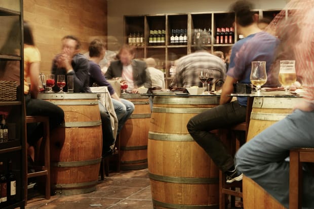 A busy wine bar and brewery, people blurred around barrel-styled tables to suggest a fast-paced setting or  passing of time.